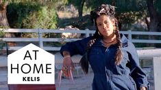 a woman standing in front of a fence with her hands on her hips and the words at home kelis