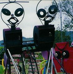 two metal sculptures with faces on them sitting in the middle of a field next to trees