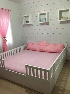 a child's bed with pink sheets and pillows in a room that has wallpaper on the walls