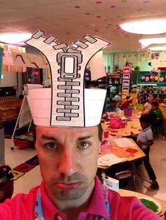 a man wearing a paper hat with a cell phone on it's head in a classroom