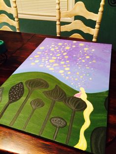 a painting on a wooden table with chairs and a green vase in the background,