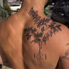 a man with a tattoo on his back has flowers growing out of the top of it