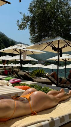 a woman laying on top of a beach next to umbrellas and chairs with trees in the background