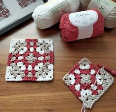 two crocheted squares sitting on top of a wooden table next to balls of yarn