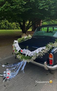 an old car is decorated with greenery and streamers as it sits on the side of the road