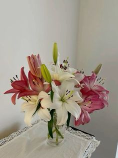 a glass vase filled with pink and white flowers on top of a lace table cloth