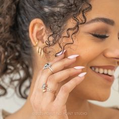 a woman with curly hair smiling and holding her hand up to her face while wearing two rings