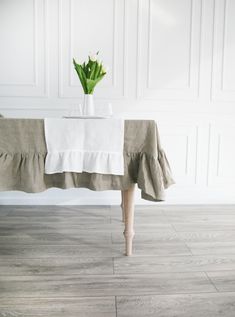 a white vase with flowers sitting on top of a wooden table next to a wall