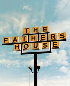 a yellow and black sign that says the fathers house on it's side under a cloudy blue sky