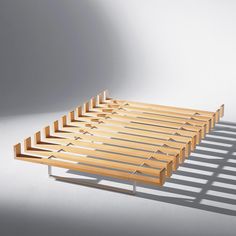 a wooden bed frame sitting on top of a white floor next to a shadow cast wall