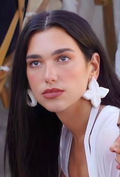 a woman with long black hair and white earrings on her neck posing for the camera