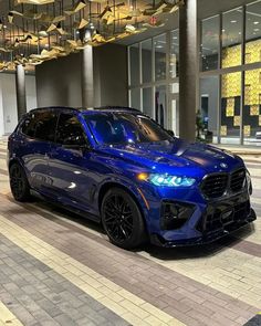 a blue bmw suv parked in front of a building with lights on it's windows