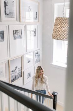 a woman standing on top of a stair case next to a wall filled with pictures