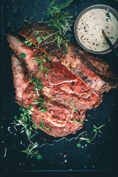 some meat is laying on a black plate next to a bowl of sauce and spoons