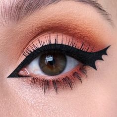 In this photo, the makeup artist has created a mesmerizing winged eyeliner with a twist: the wings are shaped like bats. The eyeshadow is a warm, burnt orange that complements the bat wings and makes the eyes pop. This simple Halloween makeup is subtle yet festive.   Photo credit by: @sophiemaykup Bat Eyeliner Tutorial, Bat Eye Makeup, Easy Halloween Eyeliner, Bat Liner, Ghost Eyeliner, Easy Halloween Eye Makeup, Halloween Eyeliner Looks, Bat Wing Eyeliner, Bat Eyeliner