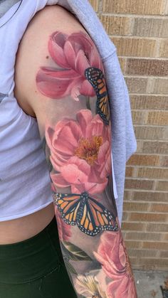 a woman's arm with pink flowers and butterflies on it, next to a brick wall