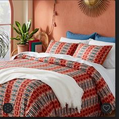 a bed in a bedroom with orange walls and red patterned bedspread on top of it