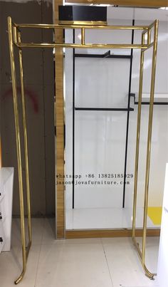 an open glass door with gold frame and metal bars on the bottom, in front of a white wall