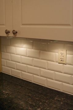 a kitchen with white cabinets and black granite counter tops is lit by the light switch