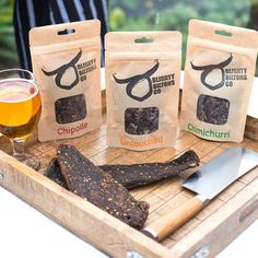 three bags of food sitting on top of a wooden tray next to a glass of beer