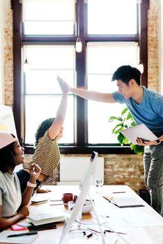 three people in an office setting, one pointing at something on the table while the other holds his arm out