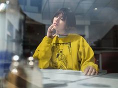 a woman sitting at a table in front of a window with her hand on her chin