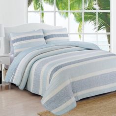 a bed with blue and white striped bedspread in front of a large window