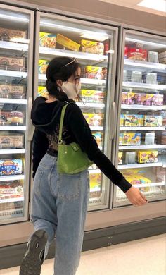 a woman wearing a face mask standing in front of refrigerators filled with food and drinks