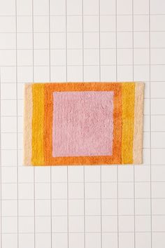 an orange and pink rug on top of a white tiled wall