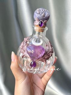 a hand holding a small glass bottle with purple decorations on it