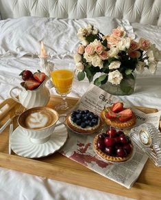 a tray topped with fruit and pastries next to a cup of coffee on top of a bed