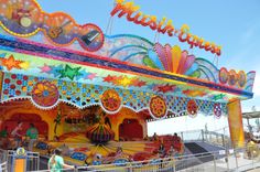 a carnival ride with colorful decorations and people walking around the carousels at an amusement park