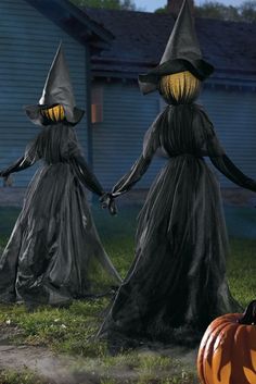 three halloween witches walking in front of a house with pumpkins on the ground and one holding hands