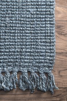 a blue rug with tassels on top of wooden floor next to wood wall