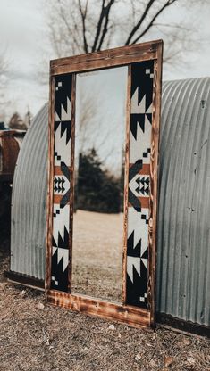 a mirror sitting on the ground next to a metal structure with a pattern on it