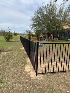 a black metal fence in front of a house with trees and grass around the perimeter