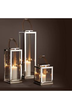 three glass lanterns with candles in them on a brown background, one is lit and the other has a handle