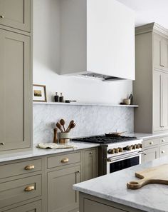 a kitchen with an oven, stove and counter tops in grey cabinets next to a wooden cutting board