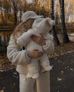 a woman holding a white teddy bear in her arms while standing next to a lake