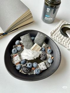 a black plate topped with blueberries and marshmallows next to an open book