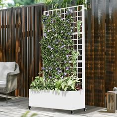 a white planter filled with purple flowers on top of a wooden floor next to a fence