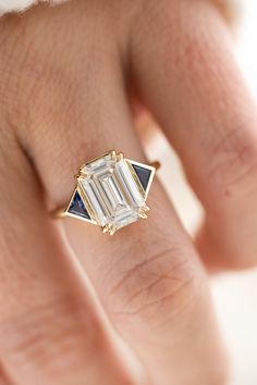 a woman's hand with a ring on it that has an emerald and blue diamond in the middle