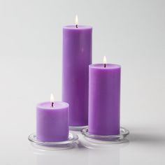 three purple candles sitting next to each other on top of a glass plate with the candle lit