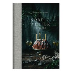 the nordic winter cookbook is on display in front of a table with candles and leaves