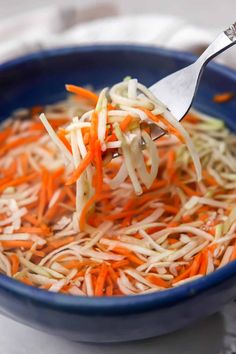 shredded carrots and cabbage in a blue bowl with a silver serving spoon on top