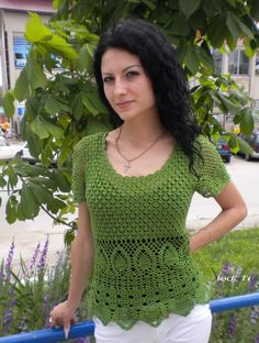 a woman standing in front of a tree wearing white pants and a green crochet top