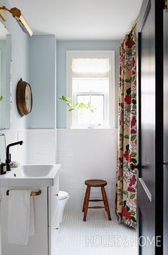 a white bathroom with floral shower curtain and stool next to the sink in front of the window