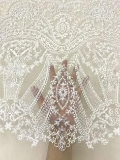 a woman's hand is holding an intricately designed white wedding veil with flowers on it