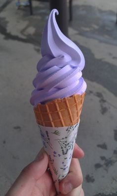 a hand holding an ice cream cone with purple icing