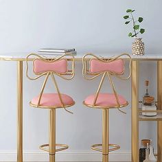 two pink and gold barstools with bows on them in front of a white wall